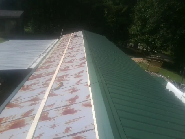 Old rusted panels beside newly installed green metal roofing — Wind Damage Roof Repair by Roofing Brothers in Bean Station