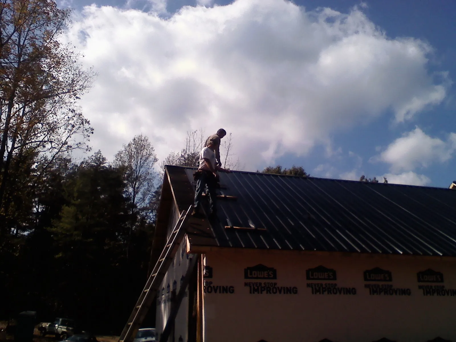 Roofer fastening dark metal panels high against a cloudy sky, from a Roof Inspection job in Bean Station