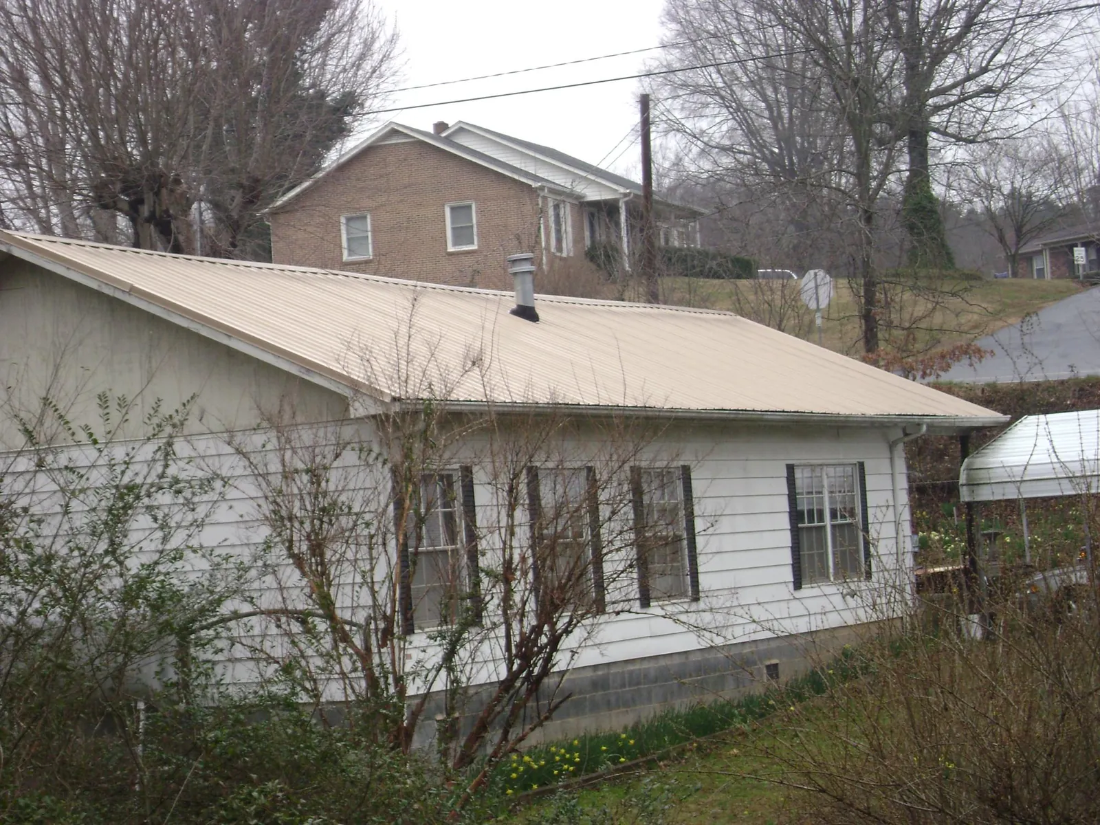 Tan metal roof on a white sided house set into a hillside — Commercial Roofing by Roofing Brothers in Bean Station