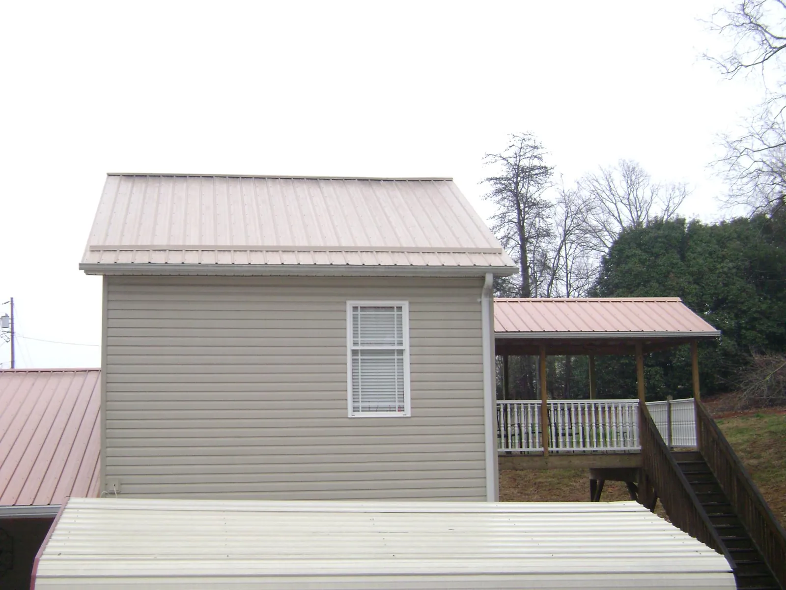 Tan metal roofs on a two story addition and attached porch, from a Roof Replacement job in Bean Station